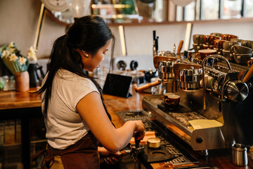 Young woman barista making cup of coffee using espresso machine