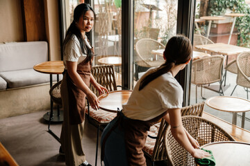 Two young waitresses cleaning the tables while working in cafe