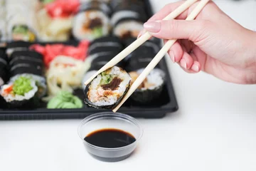 Fotobehang Sushi background. Woman hand holding chopsticks. Futomaki salmon roll. Japanese food isolated on white table. Eating sushi with dark soy sauce. Takeaway sushi lunchbox. Dipping sushi in soy sauce. © Paweł Michałowski