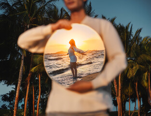 Man holding a mirror in his hand The reflection is a woman standing on the beach.
