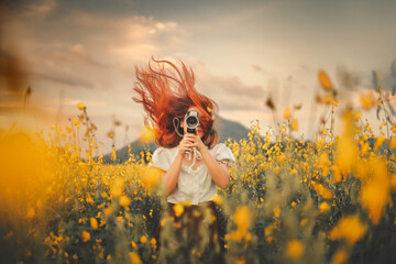 Young woman holds camera in yellow flower garden - Powered by Adobe