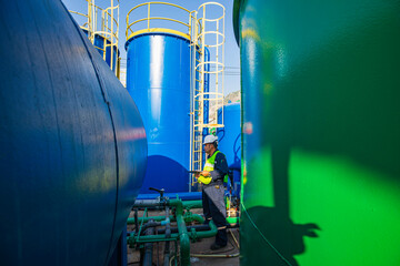 Male worker works permit industry visual inspection the row of big white tanks for petrol