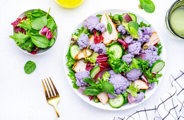 Yummy fresh salad from purple cauliflower, chicken breast, cucumbers, onion, radicchio, spinach and pumpkin seeds, white background, top view