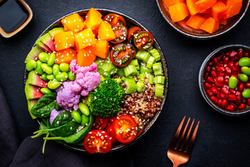 Vegan buddha bowl with pumpkin, quinoa, tomatoes, spinach, celery, radish, edamame, tofu, broccoli and seeds, black table background, top view. Vegetarian comfort healthy food