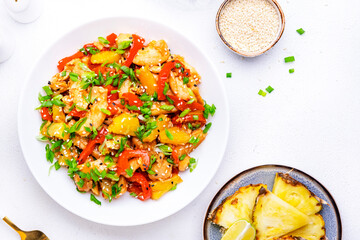 Stir fryed chicken slices with fresh pineapple, paprika, chives, soy sauce and sesame seeds. Asian cuisine dish. White table background, top view