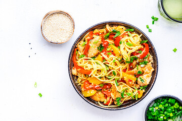 Stir fryed egg noodles with chicken, fresh pineapple, paprika, green onion, ginger, garlic, soy sauce and sesame seeds in bowl. Asian cuisine dish. White table background, top view