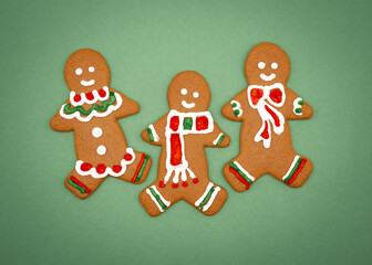 Three colorful gingerbread men cookies with green and red frosting on a green background 