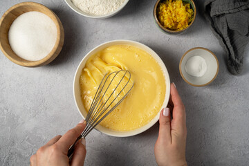 Woman's hands whisking dough, baking process of an orange cake. Ingredients on the table - wheat...