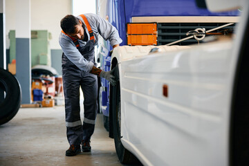 Mechanic checking truck tires while working in garage. - obrazy, fototapety, plakaty
