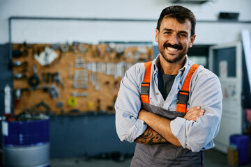 Happy truck mechanic with arms crossed in garage looking at camera.