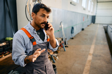 Auto mechanic talking on cell phone while working at repair shop.