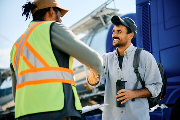 Happy truck driver greeting freight transportation manager on parking lot.