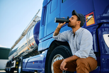 Truck driver drinking water from bottle on parking lot.