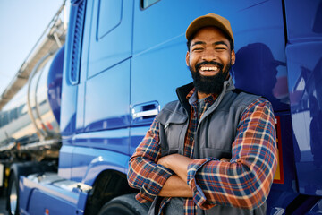 Cheerful black truck driver leaning on his vehicle and looking at camera.
