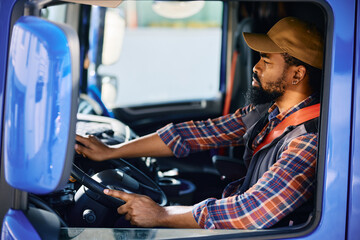 Black professional driver behind steering wheel in truck's cabin.