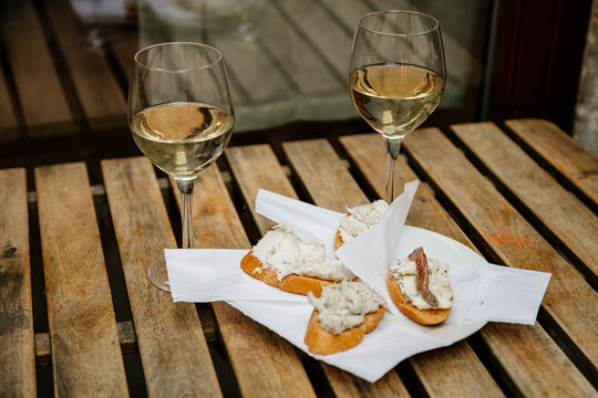 Venice, Italy, 12 February 2023:  Cichetti Venetian tapas with cod mash, cafe restaurant Bacari, Traditional Appetizers snacks accompanied with two glass of white wine, bar food, wooden table