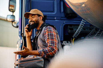 Happy black truck driver talks on cell phone on parking lot.