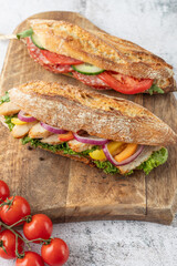 Crusty baguette submarine sandwiches on wooden board.
