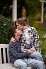 Fototapeta premium Autumn Romance: Young Couple Embracing and Kissing on Park Bench. Young couple kissing and rejoices at the lake. lovely young couple kissing outdoors in autumn. Embraced in Autumn's Warmth: Couple's