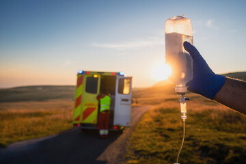 Close-up hand of paramedic holding IV drip against ambulance car of emergency medical service....