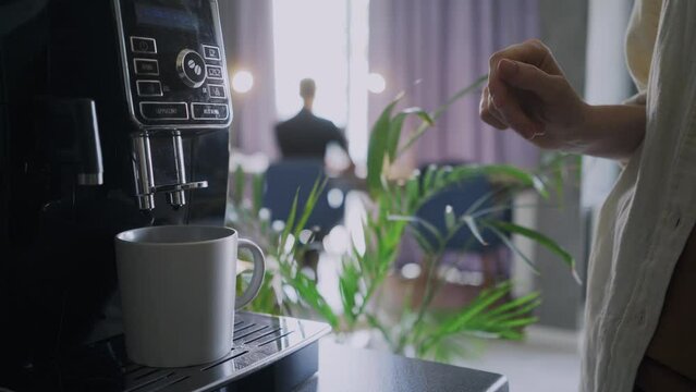 Detail view faceless woman put empty mug in to home coffee machine and choose the settings for brewing coffee. People working in small cozy coworking in morning time