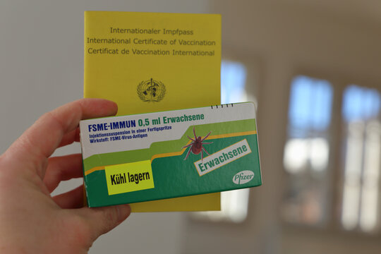 Hand holding Pfizer FSME vaccine for adults and yellow international vaccination certificate.
