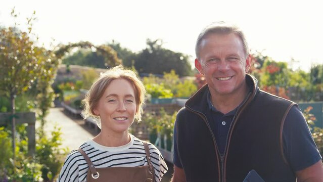 Portrait of woman wearing apron and mature man working outdoors in garden centre holding digital tablet - shot in slow motion