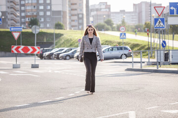young girl with sunglasses in jacket posing near modern office building with mirrored walls in parking lot with road signs © hiv360