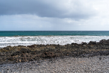 Fototapeta na wymiar Turbulent Waves Crashing Against Rocky Shoreline Under a Cloudy Sky