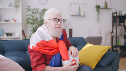 Close-up of a man in his 60s wrapped in the French flag, enthusiastically cheering for the football...