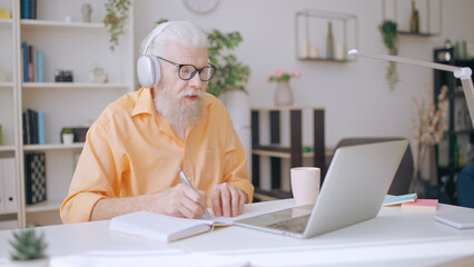 Senior man converses with his online tutor, dedicatedly studying at home as a mature student