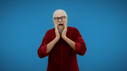 Stylish senior man holds his head in his hands in surprise, overwhelmed by shocking news and...