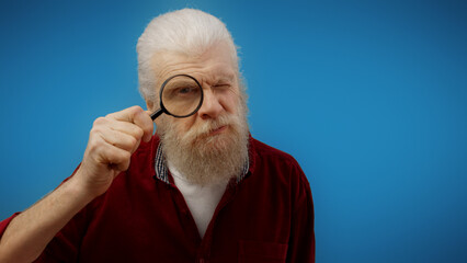 Curious man in his 60s holds a magnifying glass, probing and spying like a detective