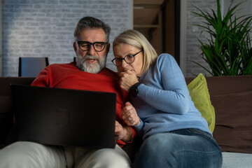 Senior husband and wife watching a horror movie on laptop in the evening at home