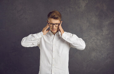 Tired man doing head massage trying to get rid of his headache. Stressed exhausted young guy in glasses doing breathing exercise and rubbing temples trying to calm down, ease pain and relieve stress