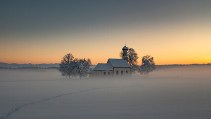 Bavarian church of Raisting with trees and snow during winter and sunset, snow field in the...