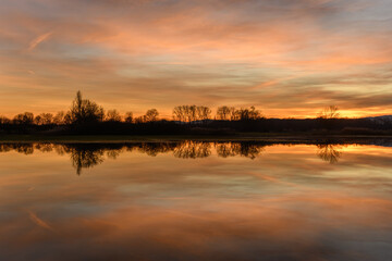 Fototapeta na wymiar Trees reflecting in the water at sunset. Winter landscape red and orange sky.
