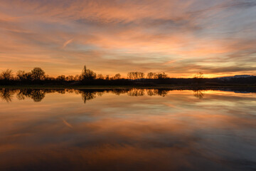 Trees reflecting in the water at sunset. Winter landscape red and orange sky.