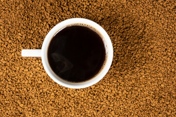 A cup of hot instant coffee on a background of freeze-dried granules