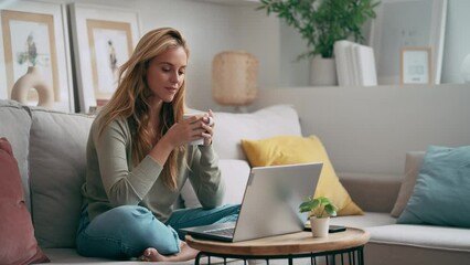 Video of beautiful young woman working with her laptop while drinking a cup of coffee sitting on a couch at home - Powered by Adobe