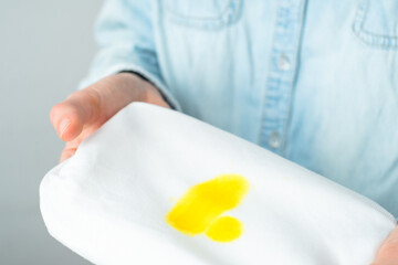 Unrecognizable woman hands holding white clothes with a yellow stain. Spoiled clothes. daily life...