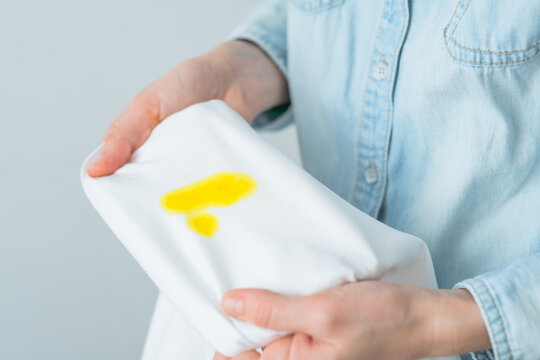 Unrecognizable woman holding white clothes with a yellow stain. Spoiled clothes. daily life stain concept. top view.