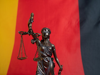 Bronze statue of justice with the German flag in the background. German law concept.