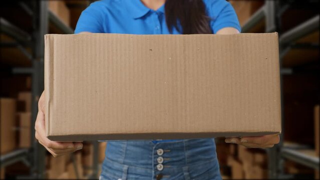 Close Up Of A Female Courier In Blue Uniform Showing A Carton To Camera While Delivering It In Warehouse
