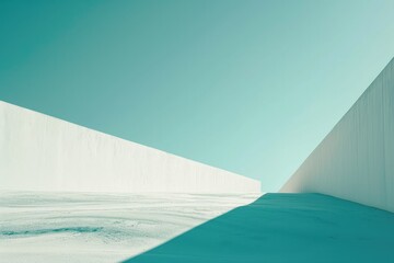 A stark white wall stands tall against the bright blue sky, casting a deep aqua shadow on the outdoor ground below
