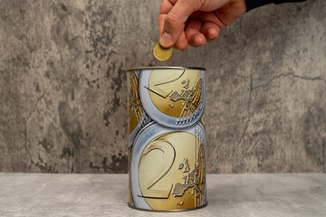 Man's hand putting a 50 cent coin into a metal piggy bank with euro symbols to save money. On a...