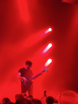 Musician guitarist plays guitar solo in red light of spotlights on stage. An unidentified person