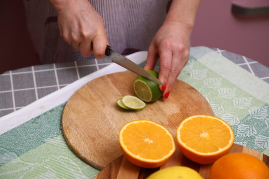 Hand Holding Knife Cut Lime on Chopping Board in Kitchen. - Powered by Adobe