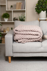 Knitted large plaid blanket in dusty rose light grayish-red color on the sofa.