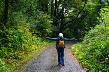 Woman opening her arms in the middle of the road in a lush landscape of nature and trees with a...